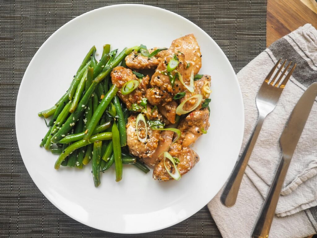 A delicious serving of sesame chicken with fresh green beans on a white plate, perfect for dinner.