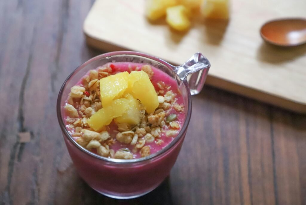 Top view of a vibrant smoothie bowl with pineapple chunks and granola on a wooden table.