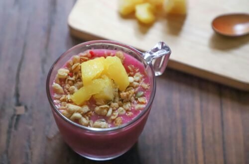 Top view of a vibrant smoothie bowl with pineapple chunks and granola on a wooden table.