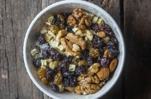 Top view of a bowl with mixed nuts and dried fruits on a rustic wooden table.