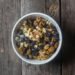 Top view of a bowl with mixed nuts and dried fruits on a rustic wooden table.