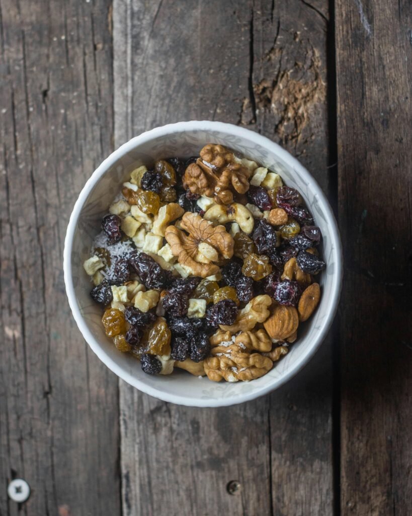 Top view of a bowl with mixed nuts and dried fruits on a rustic wooden table.