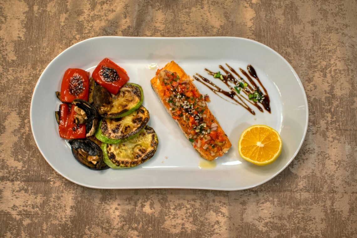 Gourmet grilled salmon served with roasted vegetables and lemon slice on a white plate.