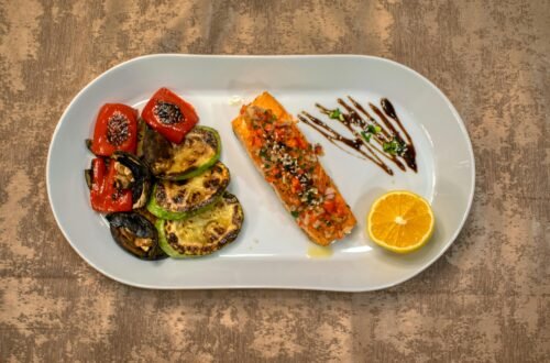 Gourmet grilled salmon served with roasted vegetables and lemon slice on a white plate.