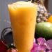 Delicious tropical fruit smoothie in a clear glass mug surrounded by fresh fruits and flowers.