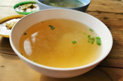 Delicious homemade soup garnished with scallions in a bowl on a rustic wooden table.