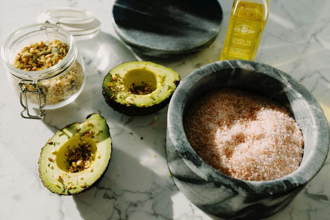 A close-up shot with avocado, pink salt, seeds, and olive oil combining for a healthy meal.