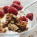 Close-up of a breakfast bowl with yogurt, fresh raspberries, and granola.