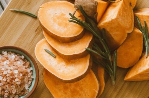 Freshly sliced sweet potatoes on a chopping board with Himalayan salt and rosemary.