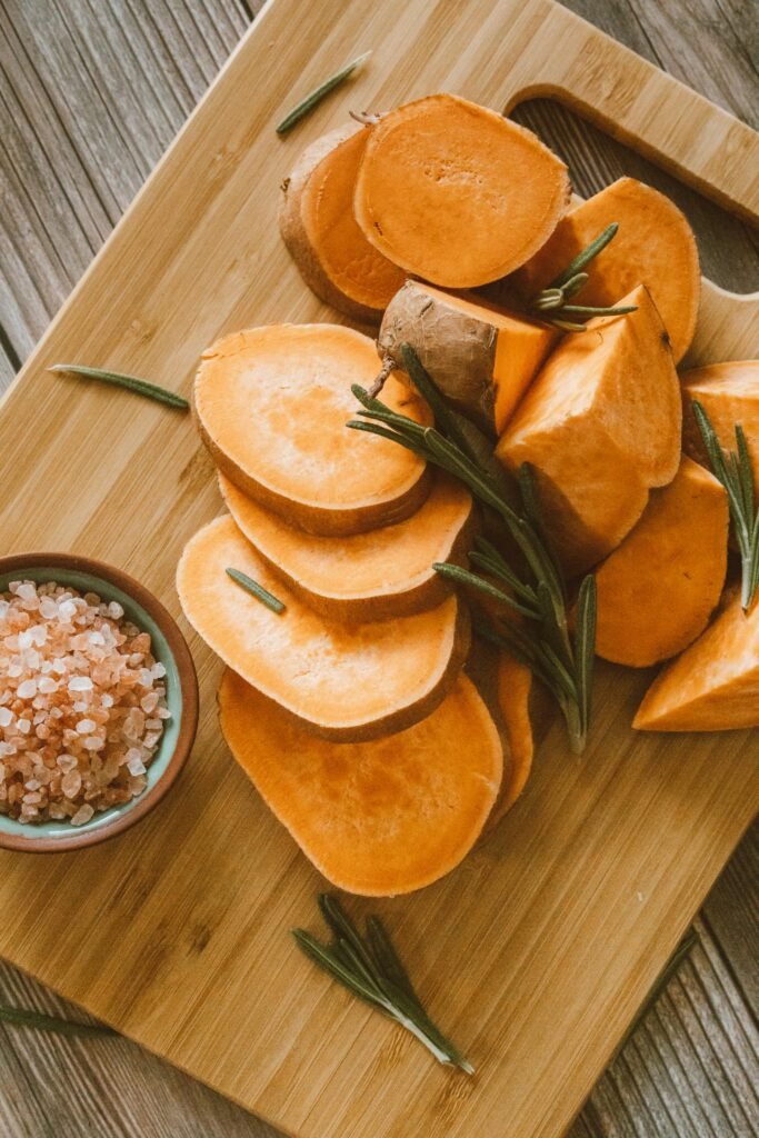 Freshly sliced sweet potatoes on a chopping board with Himalayan salt and rosemary.