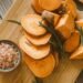 Freshly sliced sweet potatoes on a chopping board with Himalayan salt and rosemary.
