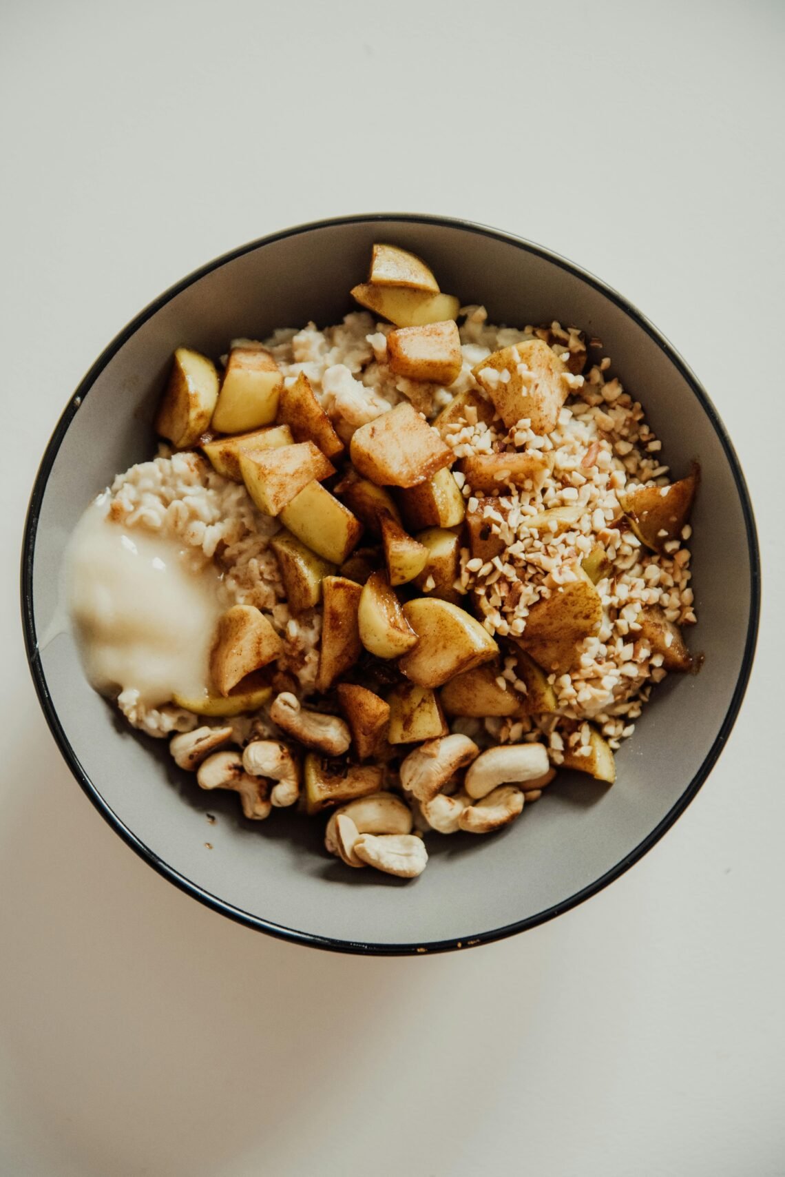 Delicious oatmeal bowl with cashews, apples, and honey on a white surface.