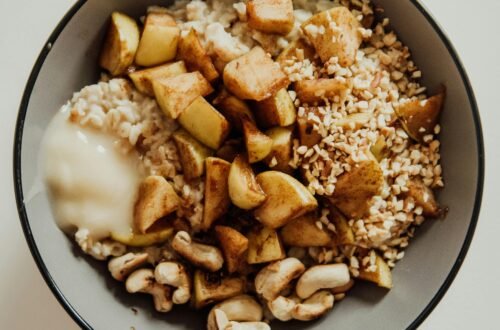 Delicious oatmeal bowl with cashews, apples, and honey on a white surface.