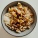 Delicious oatmeal bowl with cashews, apples, and honey on a white surface.