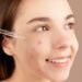 Smiling young woman applying acne treatment serum on face