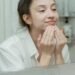 A woman applies facial cream, enjoying her skincare routine in front of a bathroom mirror.