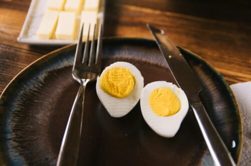 A close-up of a sliced hard boiled egg with a fork and knife on a rustic plate.