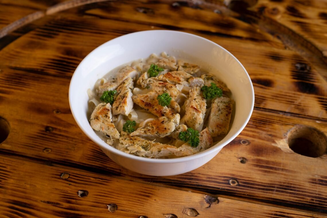 Appetizing chicken pasta dish garnished with herbs in a white bowl on rustic wooden table.