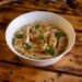 Appetizing chicken pasta dish garnished with herbs in a white bowl on rustic wooden table.