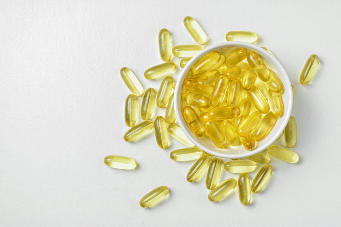 High-angle shot of omega-3 fish oil capsules in a ceramic bowl on a white background.