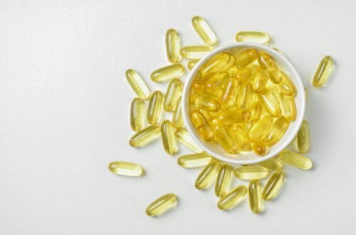 High-angle shot of omega-3 fish oil capsules in a ceramic bowl on a white background.