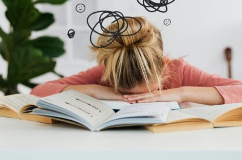 Young woman asleep over books at desk, conveying stress and mental overload.