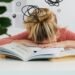 Young woman asleep over books at desk, conveying stress and mental overload.