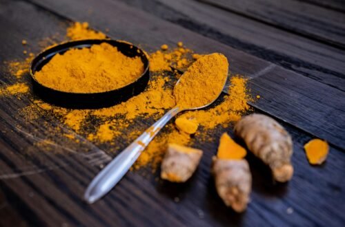 Vibrant turmeric powder and root on a dark wooden surface, emphasizing natural spices.