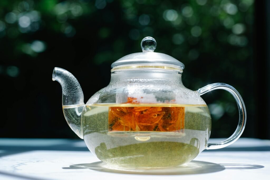 A clear glass teapot with herbal tea, captured in bright sunlight, showcasing the infusion process.