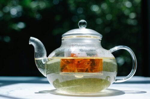 A clear glass teapot with herbal tea, captured in bright sunlight, showcasing the infusion process.