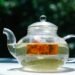 A clear glass teapot with herbal tea, captured in bright sunlight, showcasing the infusion process.