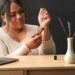 A woman uses a therapeutic essential oil roll-on at a work desk featuring a laptop and vase with flowers.