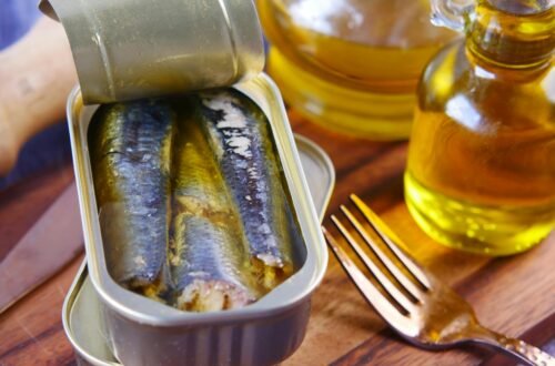 Close-up of canned sardines in olive oil with a fork on a wooden surface.